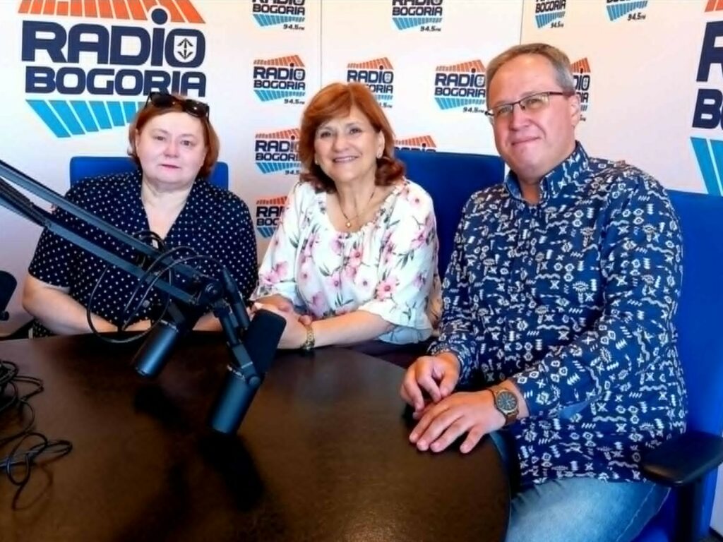 Dwie kobiety i jeden mężczyzna siedzą za mikrofonami w studiu radiowym.